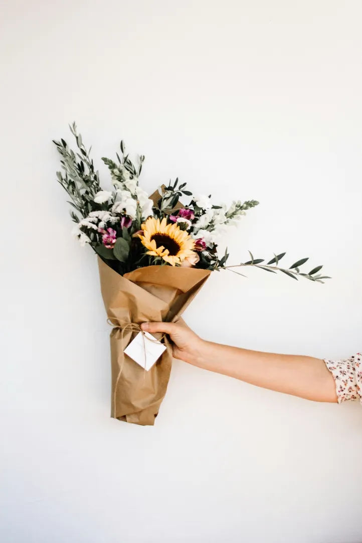 Bouquet champêtre emballé dans du papier kraft, tenu à bout de bras dans l'atelier